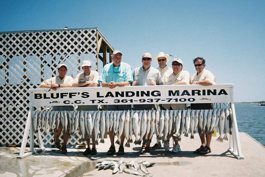 group of people standing behind a row of caught fish